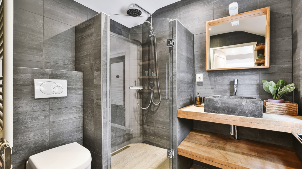 Contemporary bathroom with dark tile walls, glass shower, and wooden vanity featuring a sleek black sink.